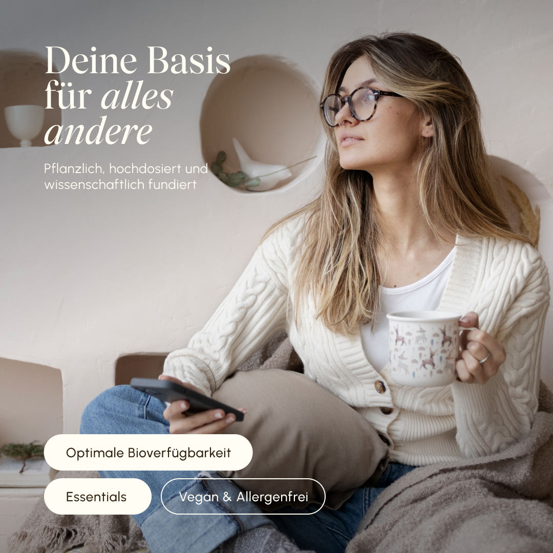 Frau mit Brille sitzt entspannt auf dem Sofa mit einer Tasse Tee und Smartphone. Text: „Deine Basis für alles andere – pflanzlich, hochdosiert und wissenschaftlich fundiert". Badges: Optimale Bioverfügbarkeit, Essentials, Vegan & Allergenfrei