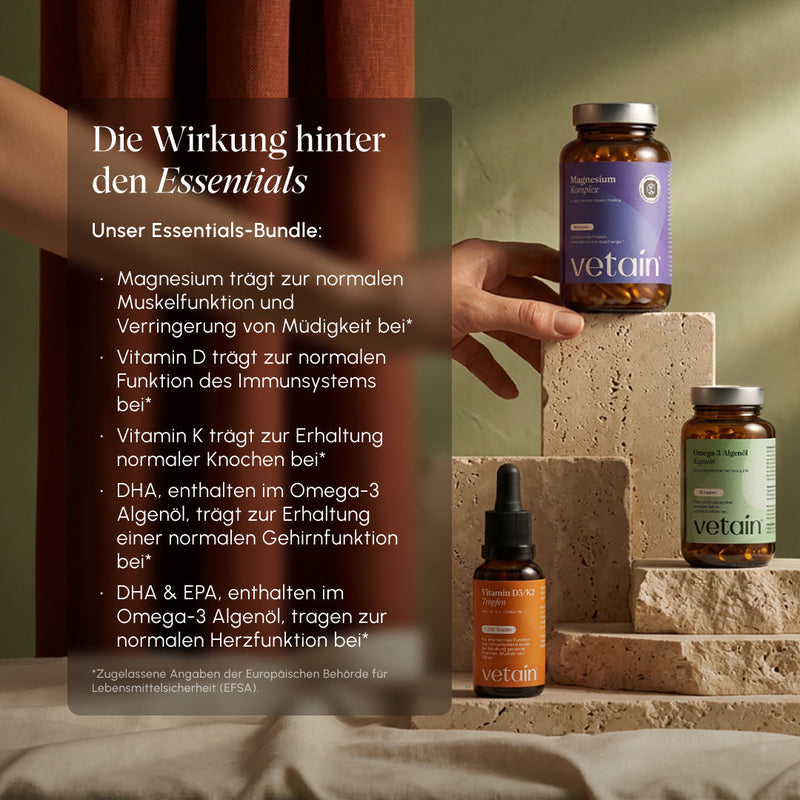 Lifestyle-Foto mit Vetain-Produkten auf Steinpodesten. Textoverlay „Die Wirkung hinter den Essentials": Magnesium für Muskelfunktion & weniger Müdigkeit, Vitamin D für Immunsystem, Vitamin K für Knochen, DHA & EPA aus Omega-3 Algenöl für Gehirn- und Herzfunktion (EFSA-zugelassene Angaben)