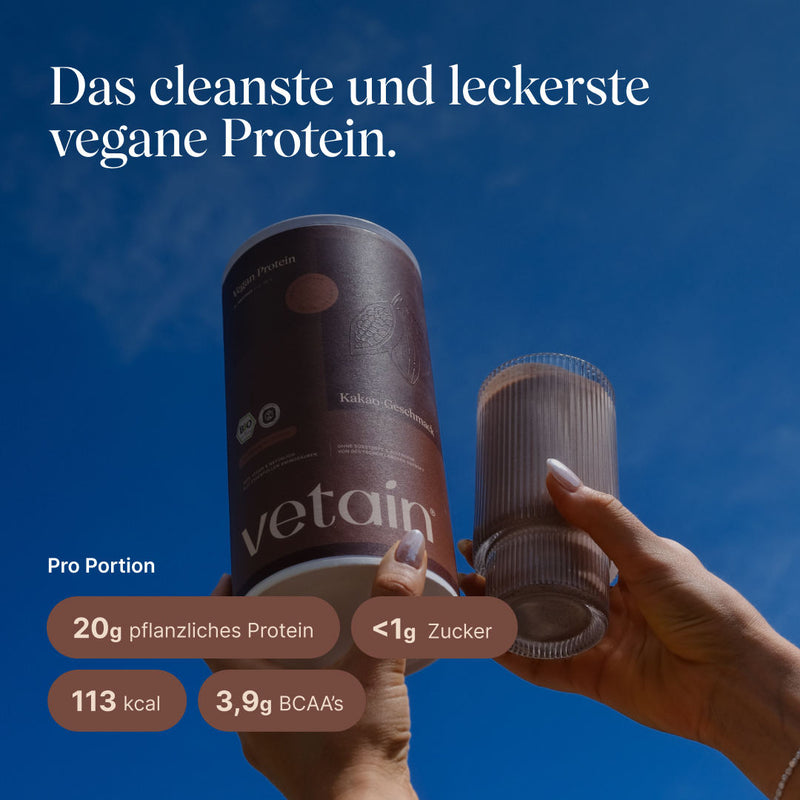 Zwei Hände halten die vetain Vegan Protein Dose (Kakao-Geschmack) und ein geripptes Glas mit Proteinshake vor blauem Himmel. Text: „Das cleanste und leckerste vegane Protein." Pro Portion: 20g pflanzliches Protein, <1g Zucker, 113 kcal, 3,9g BCAAs.