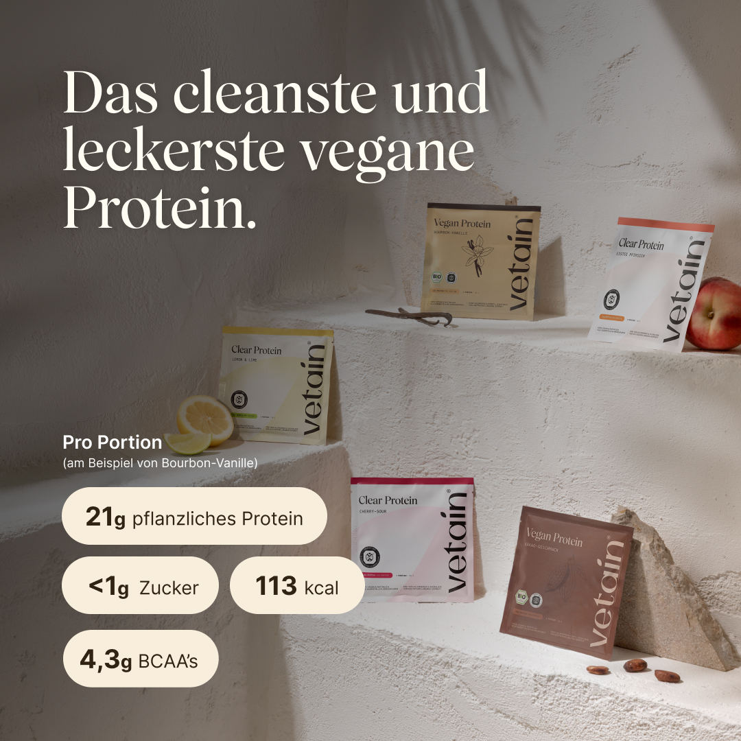 Fünf vetain Probierpackungen auf gestuften Steinabsätzen: Vegan Protein Bourbon-Vanille, Clear Protein Lemon & Lime, Clear Protein Cherry-Sour, Clear Protein Eistee Pfirsich und Vegan Protein Kakao-Geschmack, dekoriert mit Zitronenhälften und Kakaobohnen. Text: „Das cleanste und leckerste vegane Protein." Nährwerte am Beispiel Bourbon-Vanille, pro Portion: 21g pflanzliches Protein, <1g Zucker, 113 kcal, 4,3g BCAAs.