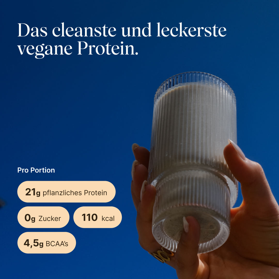 Hand hält ein geripptes Glas mit hellem Zimt-Proteinshake vor blauem Himmel. Text: „Das cleanste und leckerste vegane Protein." Pro Portion: 21g pflanzliches Protein, 0g Zucker, 110 kcal, 4,5g BCAAs.