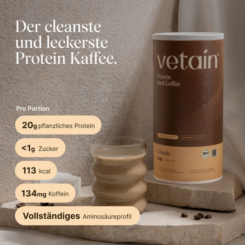 Dose vetain Protein Iced Coffee in der Sorte Classic (Medium Roast) neben einem Glas mit fertig zubereitetem Eiskaffee und einigen Kaffeebohnen auf einer Steinplatte. Überschrift: ‚Der cleanste und leckerste Protein Kaffee.' Angaben pro Portion: 20 g pflanzliches Protein, unter 1 g Zucker, 113 kcal, 134 mg Koffein, vollständiges Aminosäureprofil.