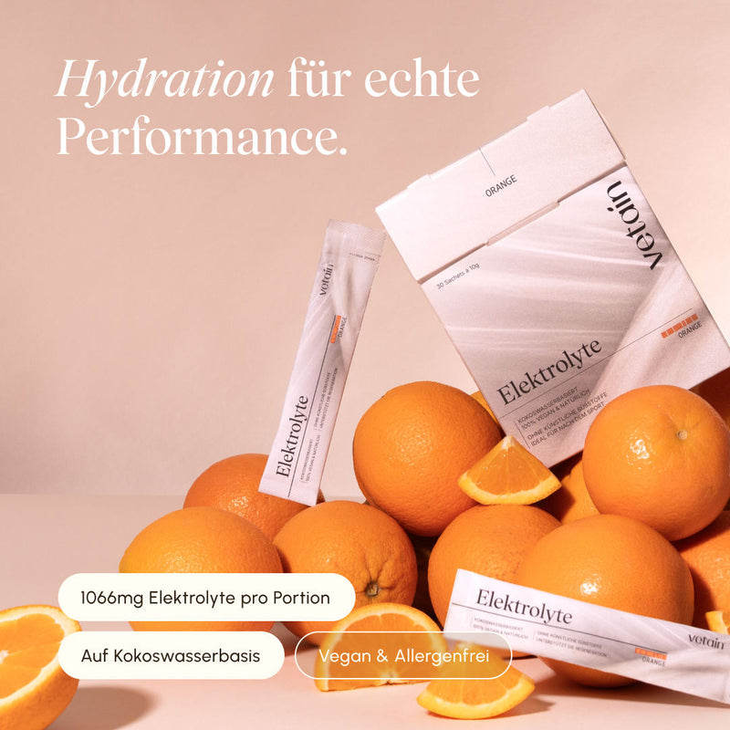 vetain Elektrolyte Orange Faltschachtel mit 30 Sachets à 10 g und einzelne Sticks vor beigem Hintergrund, umgeben von ganzen und aufgeschnittenen Orangen. Hinweise: 1066 mg Elektrolyte pro Portion, auf Kokoswasserbasis, vegan und allergenfrei.