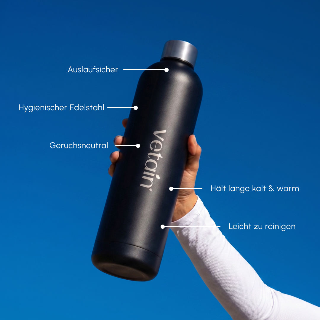 Hand holding black Vetain stainless steel water bottle against blue sky; labels: leak-proof, hygienic stainless steel, odorless, keeps cold and warm for a long time, easy to clean.