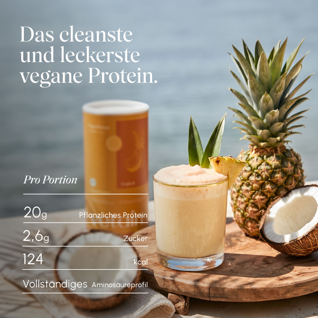Tropischer Protein-Shake im Glas mit Ananas und Kokos am Wasser, im Hintergrund die Vetain Tropical Dose; eingeblendete Werte pro Portion: 20 g pflanzliches Protein, 2,6 g Zucker, 124 kcal, vollständiges Aminosäureprofil. Text „Das cleanste und leckerste vegane Protein."