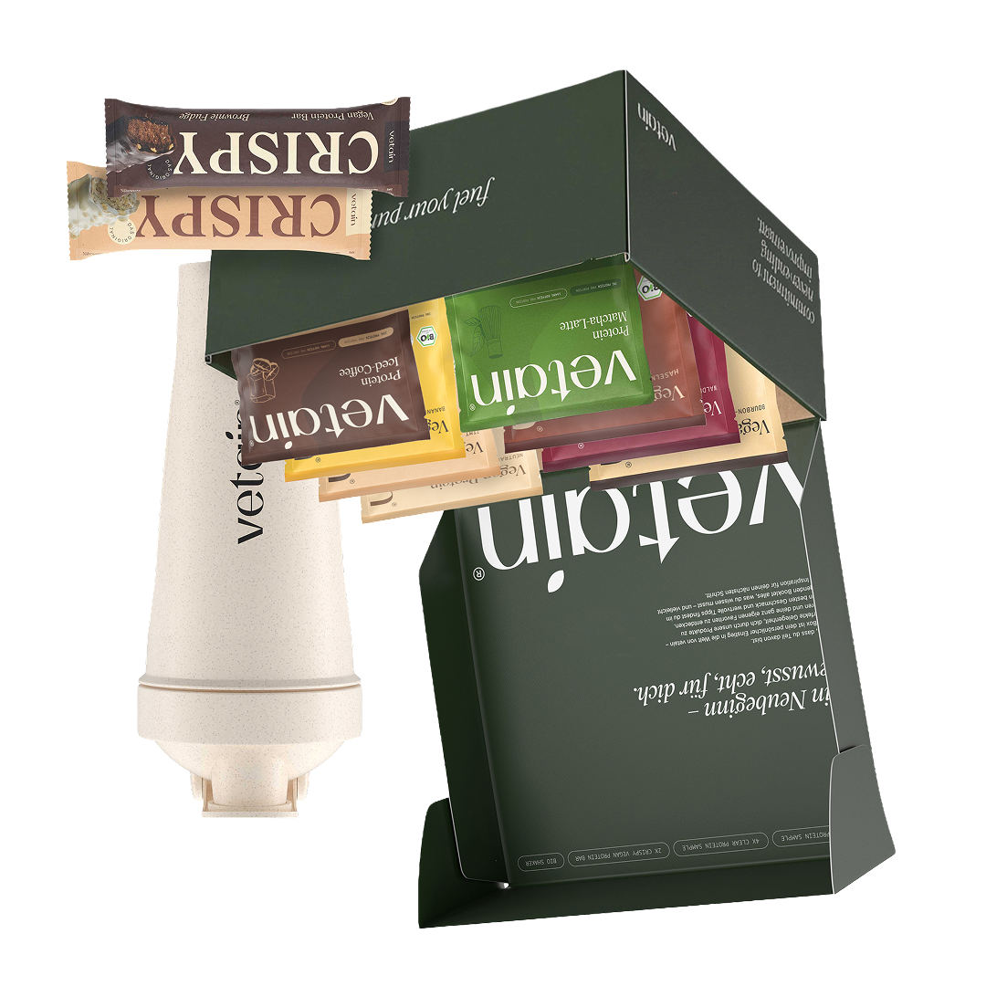 Geöffnete dunkelgrüne Vetain Probierbox mit Protein-Probensachets in verschiedenen Sorten, cremefarbenem Shaker und zwei Crispy Proteinriegeln, freigestellt vor weißem Hintergrund.