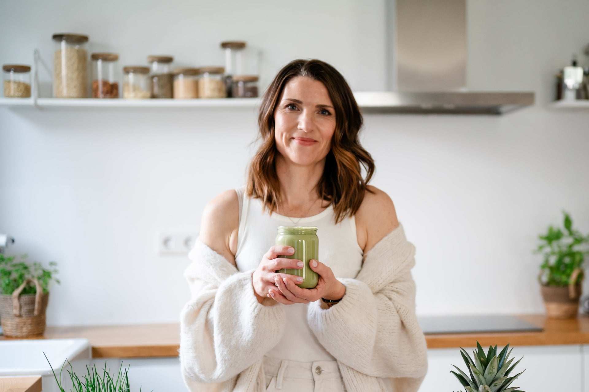 Influencerin Birgit vom Account Mama Zuckerfrei hält Proteinshake in der Hand uns steht lächelnd in der Küche