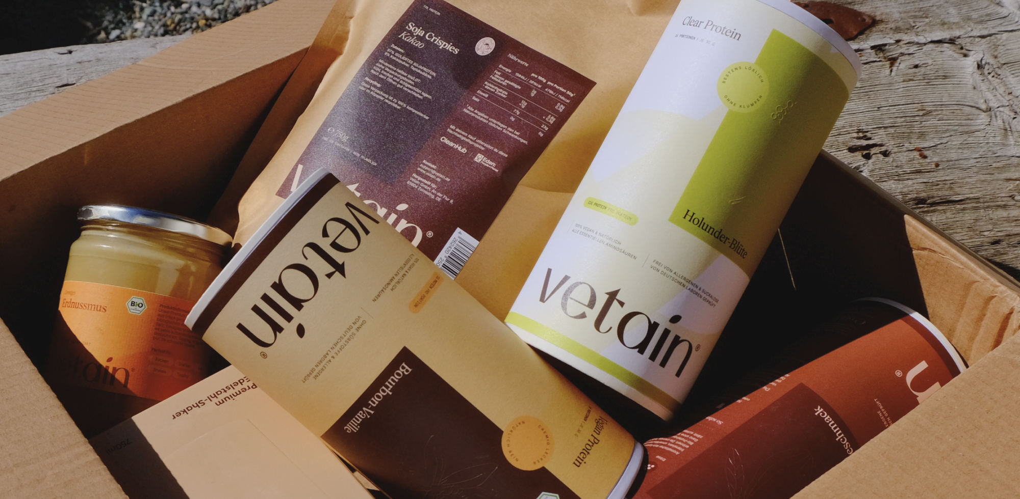 Verschiedene Vetain Produkte wie Proteinpulverdosen, Clear Dosen und Soja Crispies und Nussmus in einer Box